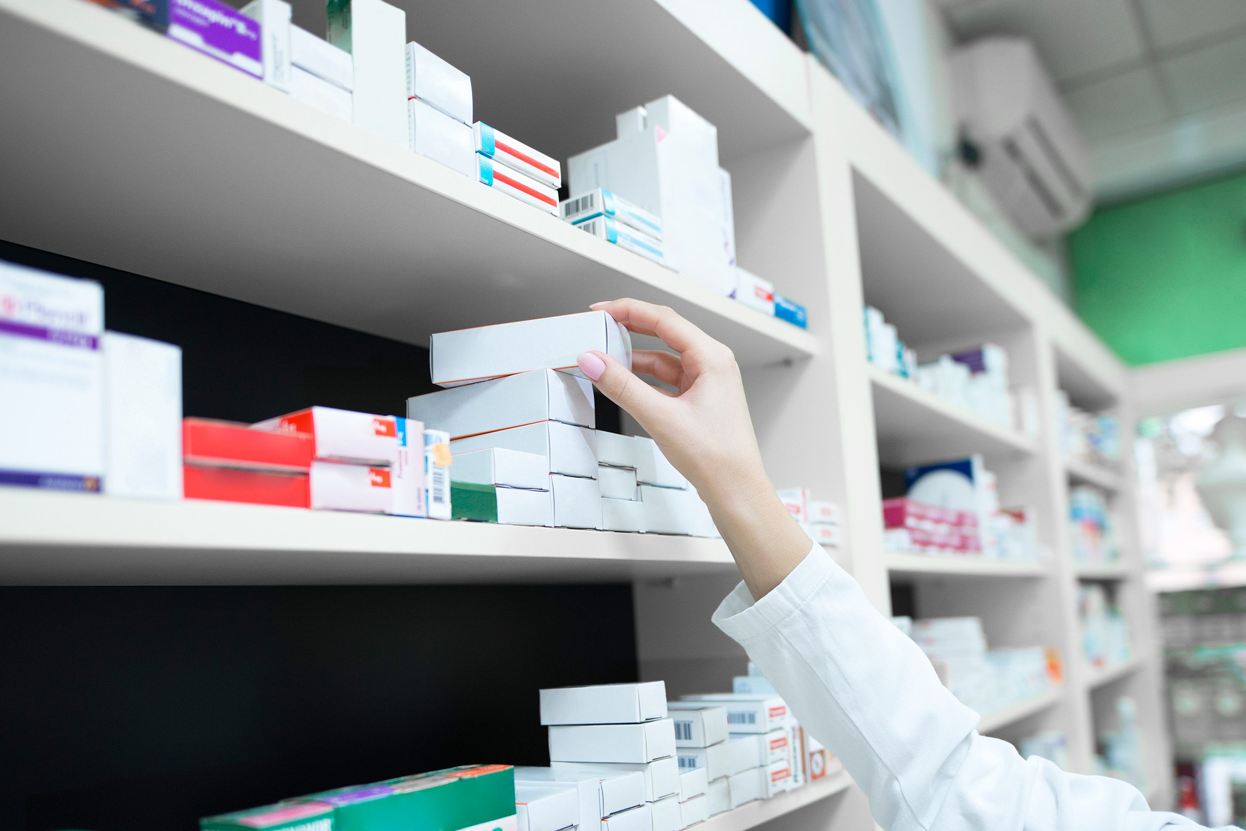 Closeup view of pharmacist hand taking medicine box from the shelf in drug store.